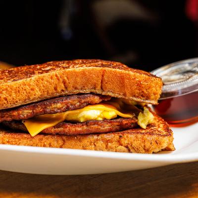 French Toast sandwich with sausage patties, scrambled eggs, cheese, and syrup.