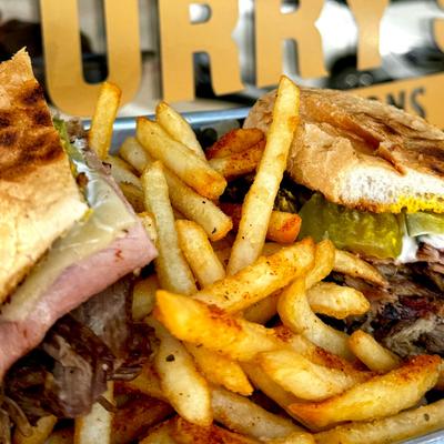 A close-up of two meat sandwiches with pickles and mustard, served with fries.