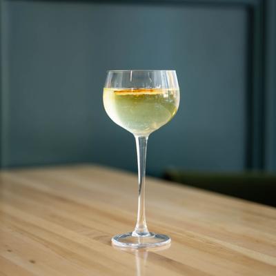 A glass of The Orient cocktail  resting on a table inside.