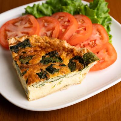 Spinach quiche slice with tomato slices and lettuce garnish.