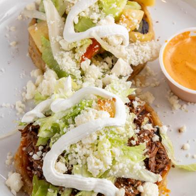 Two loaded Mexican sopes topped with lettuce, cheese, crema, and salsa.