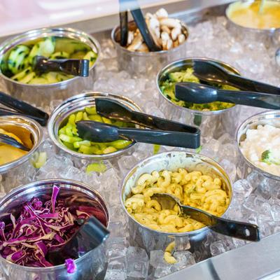Veggies, pastas, and sauces in metal bowls placed on ice.