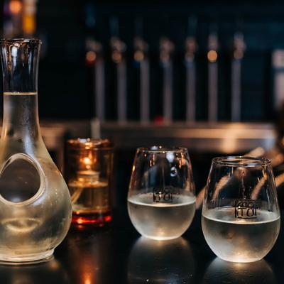 Japanese-style sake featuring glass carafe and two tumblers with restaurant signage.