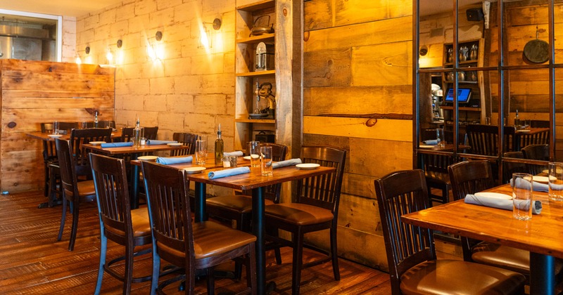 Interior, wooden tables and chairs, light colored textured walls, and soft wall lighting