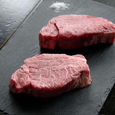 Two raw marbled steaks sit on a dark slate surface, with a small pile of coarse salt nearby.