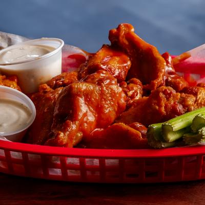 Buffalo wings with celery and dipping sauces in a red basket.