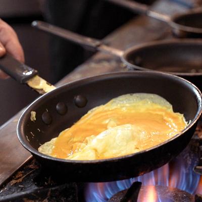 Chef flipping an omelet in a black frying pan over gas stove flames