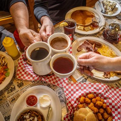 Three people clinging cups with hot drinks over the table.