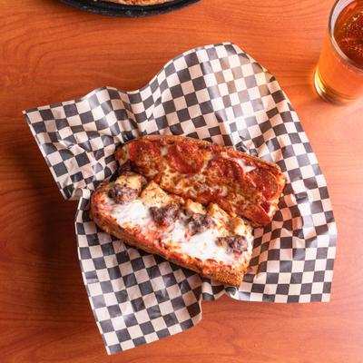 All Meat Sub sandwich on checkered paper liner, alongside a glass of beer.