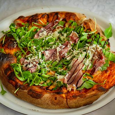 Pizza topped with proschutto, arugula, grated cheese and balsamic glaze.
