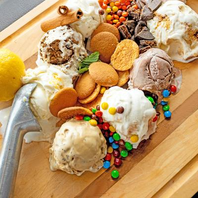 Scoops of ice cream with toppings like cookies, candy, and cinnamon, on a wooden board.