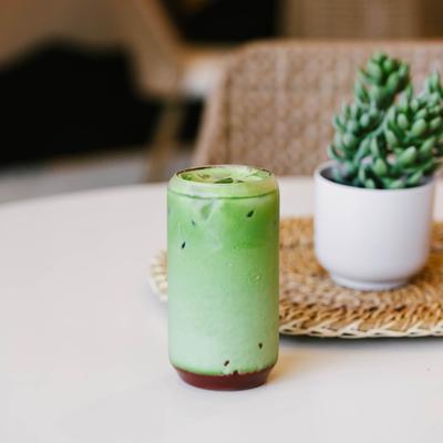 A frothy green matcha latte sits on a white table beside a small potted succulent.