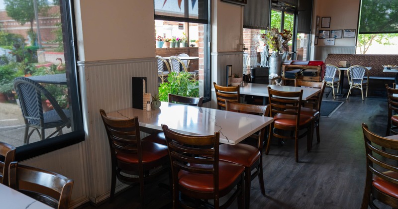 Interior,  wooden tables, brown chairs, and large windows overlooking an outdoor patio
