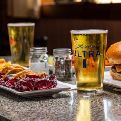 Glass of golden lager beer beside potstickers and a burger on a granite countertop.