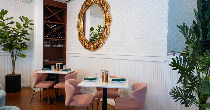 Interior, tables for three, ready for guests, plant decoration, large mirror on a brick wall