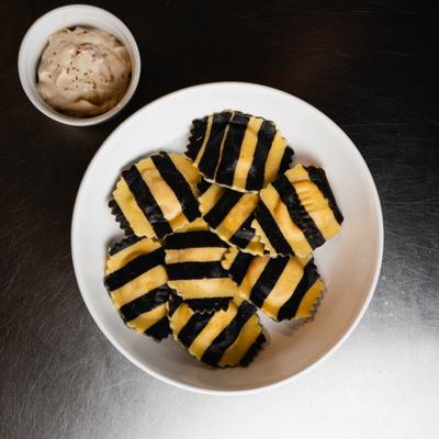 Black-and-yellow striped ravioli served with a side of creamy sauce.