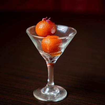 Two sweet fried dough balls in syrup, served in a martini glass.