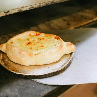 Ajaruli Khachapuri - Georgian cheese bread - being removed from a pizza oven on a peel.