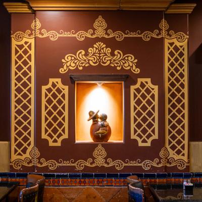 Decorative wall with gold-colored patterns and a recessed niche with a lit sculpture.