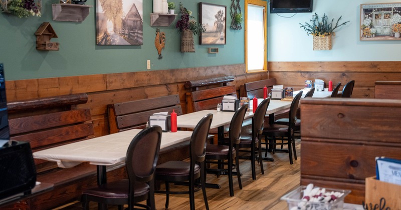 Rustic restaurant dining room with teal walls, wooden benches, decorated tables, and country-style wall art
