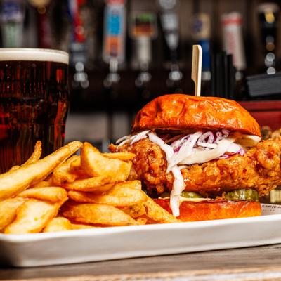 Hot Honey Chicken Sandwich served with fries and a glass of dark beer.