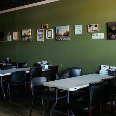 Interior with table seating and a olive green wall adorned with various framed signs.