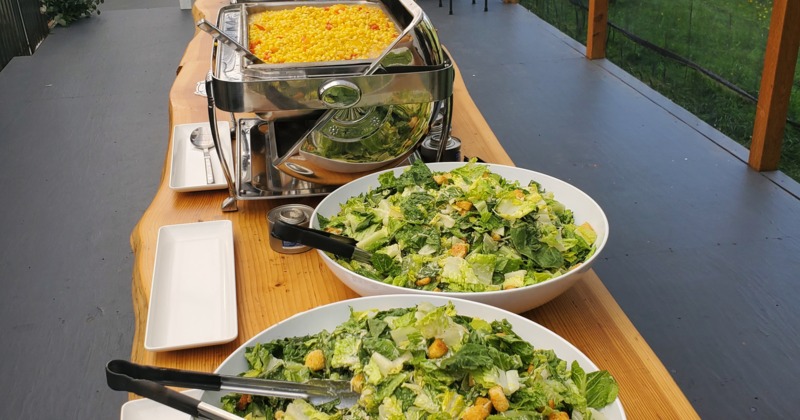 Buffet table with Caesar salads and corn in an outdoor setting