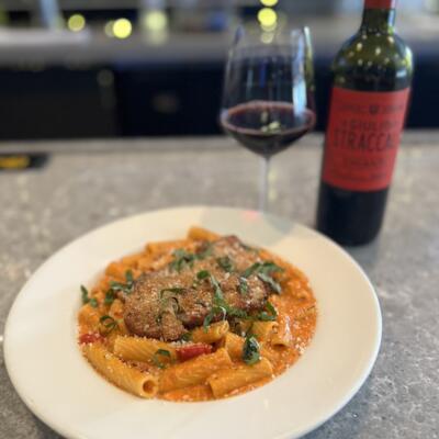 A plate of creamy rigatoni pasta with a breaded cutlet, accompanied with red wine.