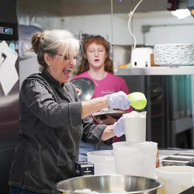 The owner with gloves measuring flour into a container.