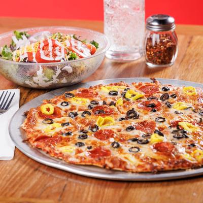 A pepperoni pizza topped with olives and peppers on a metal tray beside a fresh salad in a bow.