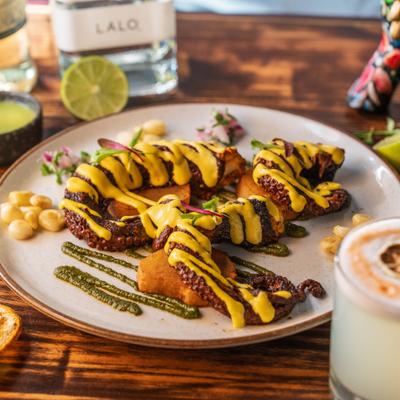 Grilled octopus with yellow and green sauces served beside a fresh cocktail.