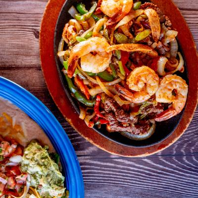 Shrimp and meat fajitas with onions and peppers on an oval platter.