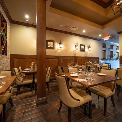 An elegantly set dining room with wooden tables and chairs, brick accent wall, and warm lighting.