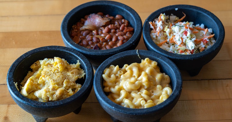 Sides of mac and cheese, baked beans, coleslaw, and cornbread