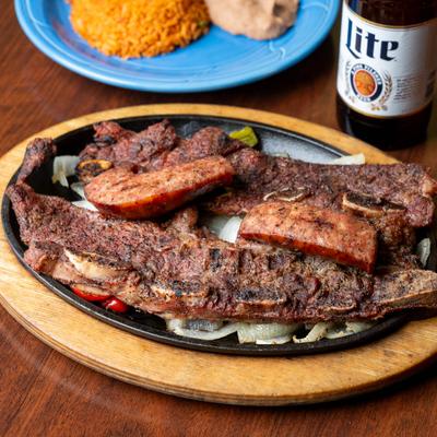 Grilled beef ribs and sausage served on a sizzling platter with grilled onions.