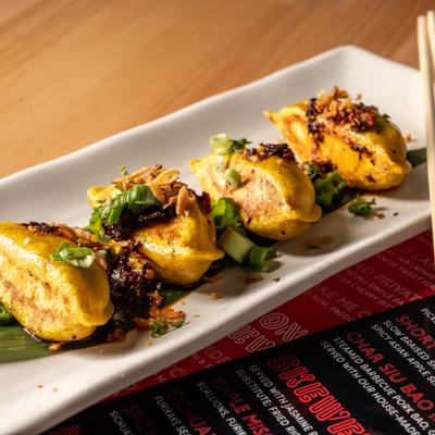 Spicy pork gyoza served on a banana leaf, garnished with sliced scallions.