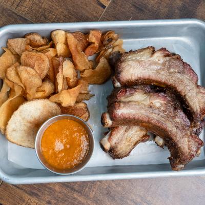 Baby-back ribs with a side of house potato chips and dipping sauce.