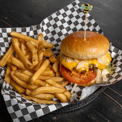 Burger with melted cheese, a tomato slice, and a side of fries served on checkered paper.