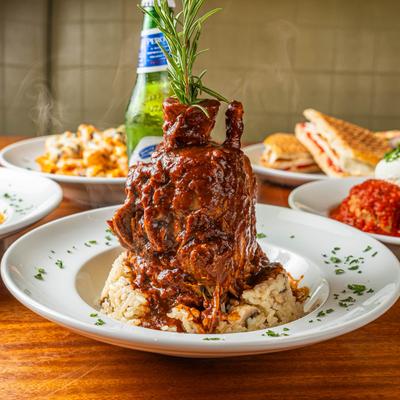 Braised lamb shank in rich sauce over rice, garnished with rosemary.