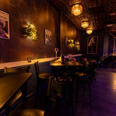 Dimly lit bar interior with patterned wallpaper and high-top tables.