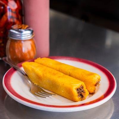 Two tamales on a plate with cayenne pepper powder in the background.
