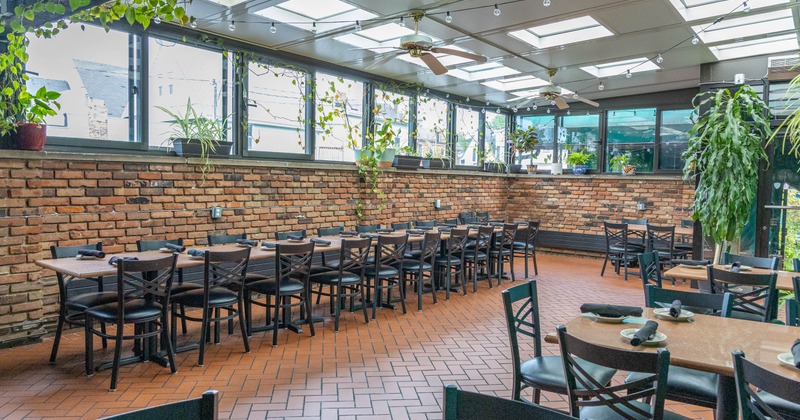 Inside, spacious dining area with brick walls, large windows, hanging plants, tables and chairs