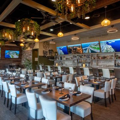 Interior with set tables, white chairs, TVs, pendant lights, and a bar.