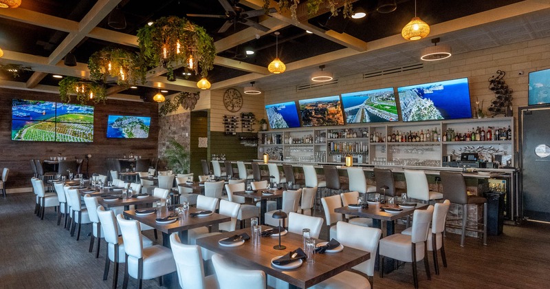 Interior with set tables, white chairs, TVs, pendant lights, and a bar