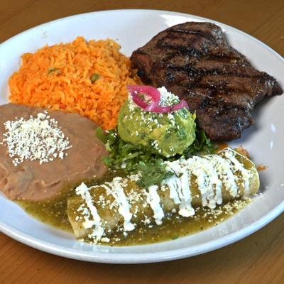 Enchilada smothered in green sauce, with steak, guacamole, rice, and beans.