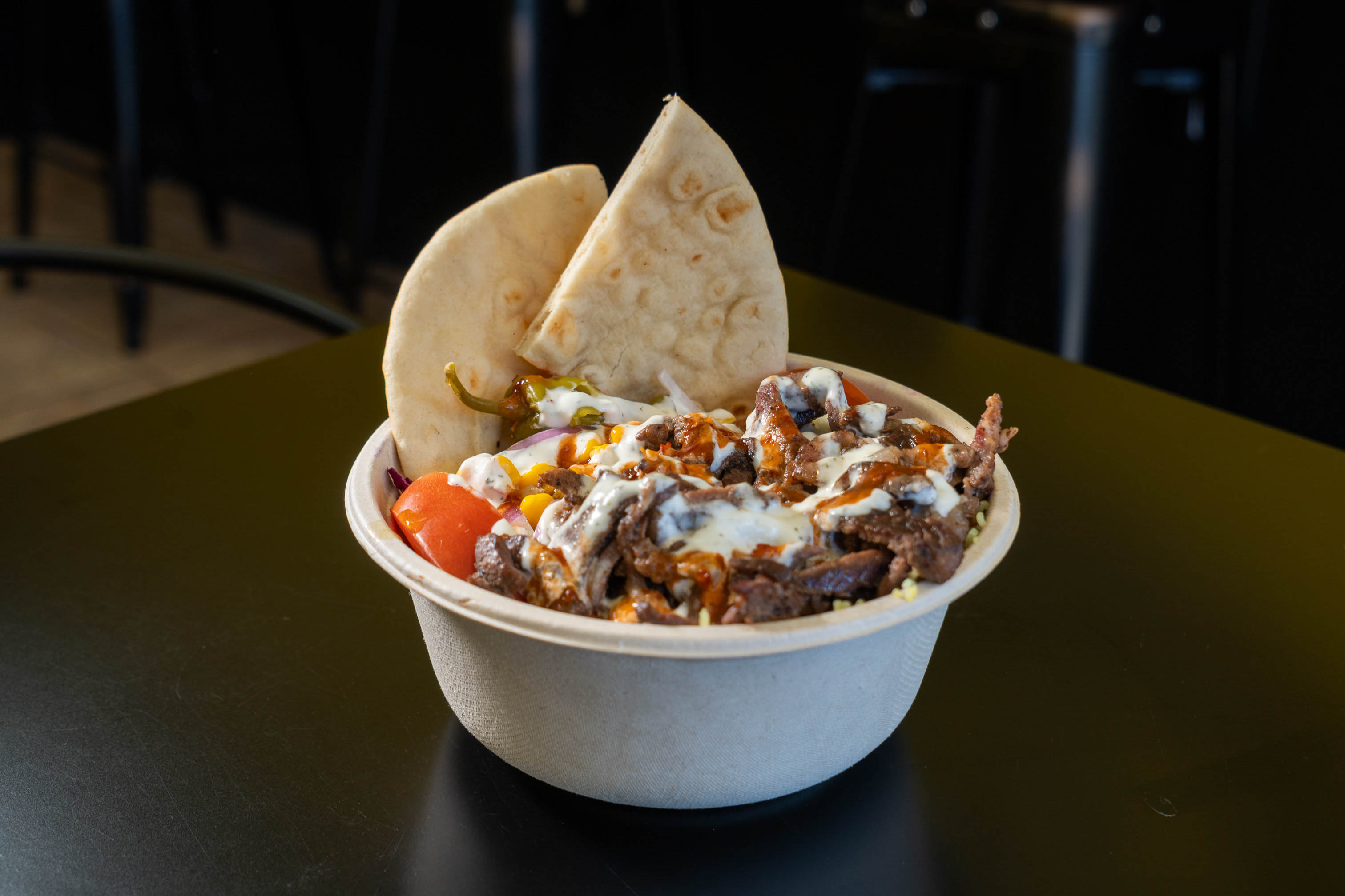 Beef shawarma bowl with tomato, corn, pita bread, and yoghurt-based sauce