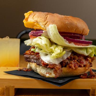 Bacon Cheeseburger served on a wooden board with a drink in the background.