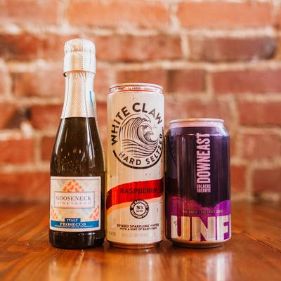 Three distinct alcoholic beverages stand lined up against a brick wall