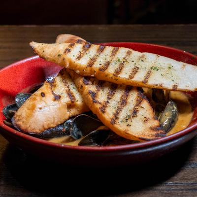 Curried mussels served with grilled bread in a red bowl.