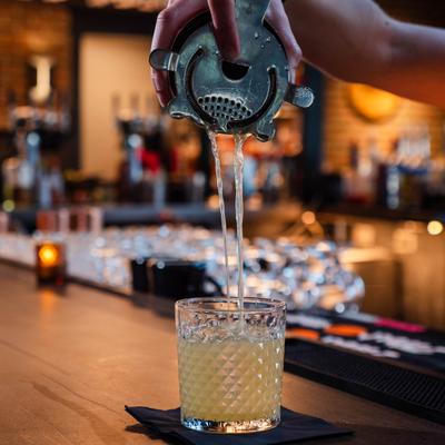 Bartender straining a cocktail into a textured glass at the bar.